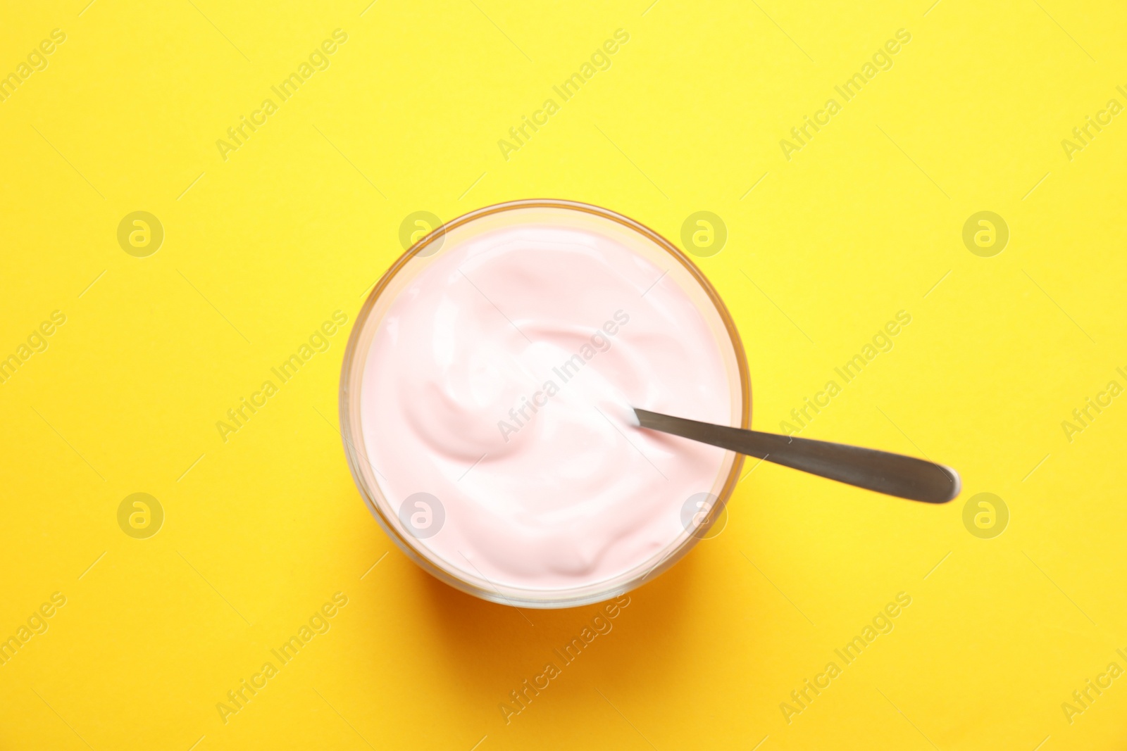 Photo of Glass bowl with creamy yogurt and spoon on color background, top view