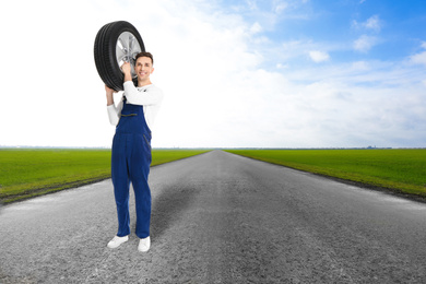 Image of Mechanic with car tire on asphalt highway outdoors, space for text