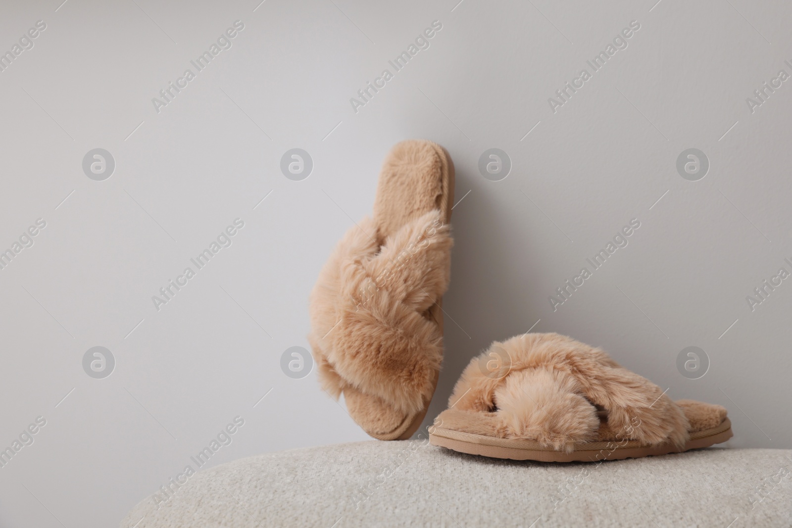 Photo of Soft beige slippers near grey wall, space for text