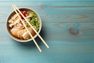 Photo of Delicious ramen with meat in bowl and chopsticks on light blue wooden table, top view. Space for text