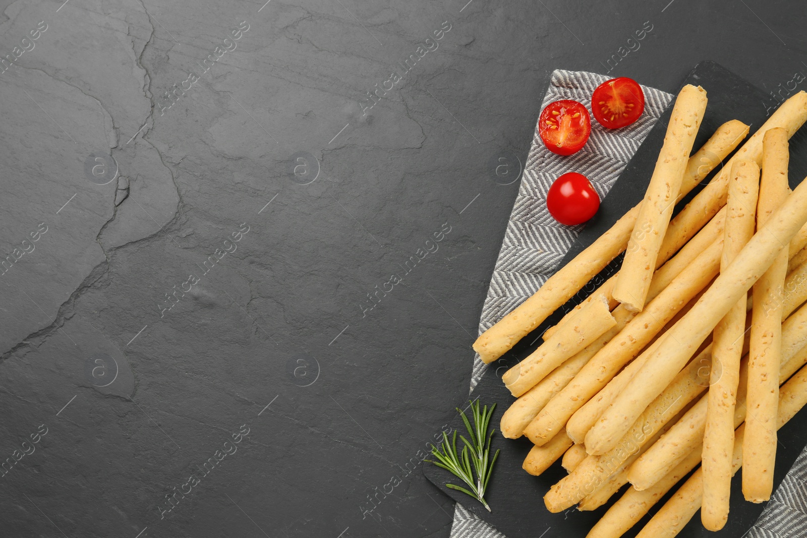 Photo of Delicious grissini with rosemary and tomatoes on black table, flat lay. Space for text