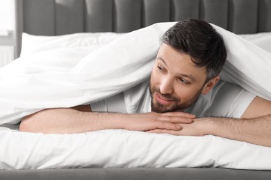 Happy man under blanket on soft bed