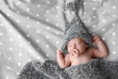 Cute newborn baby in warm hat sleeping on bed, top view. Space for text