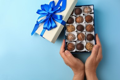 Woman with box of delicious chocolate candies on light blue background, top view. Space for text