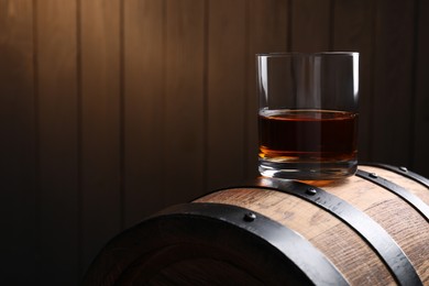Photo of Glass of tasty whiskey on wooden barrel, space for text