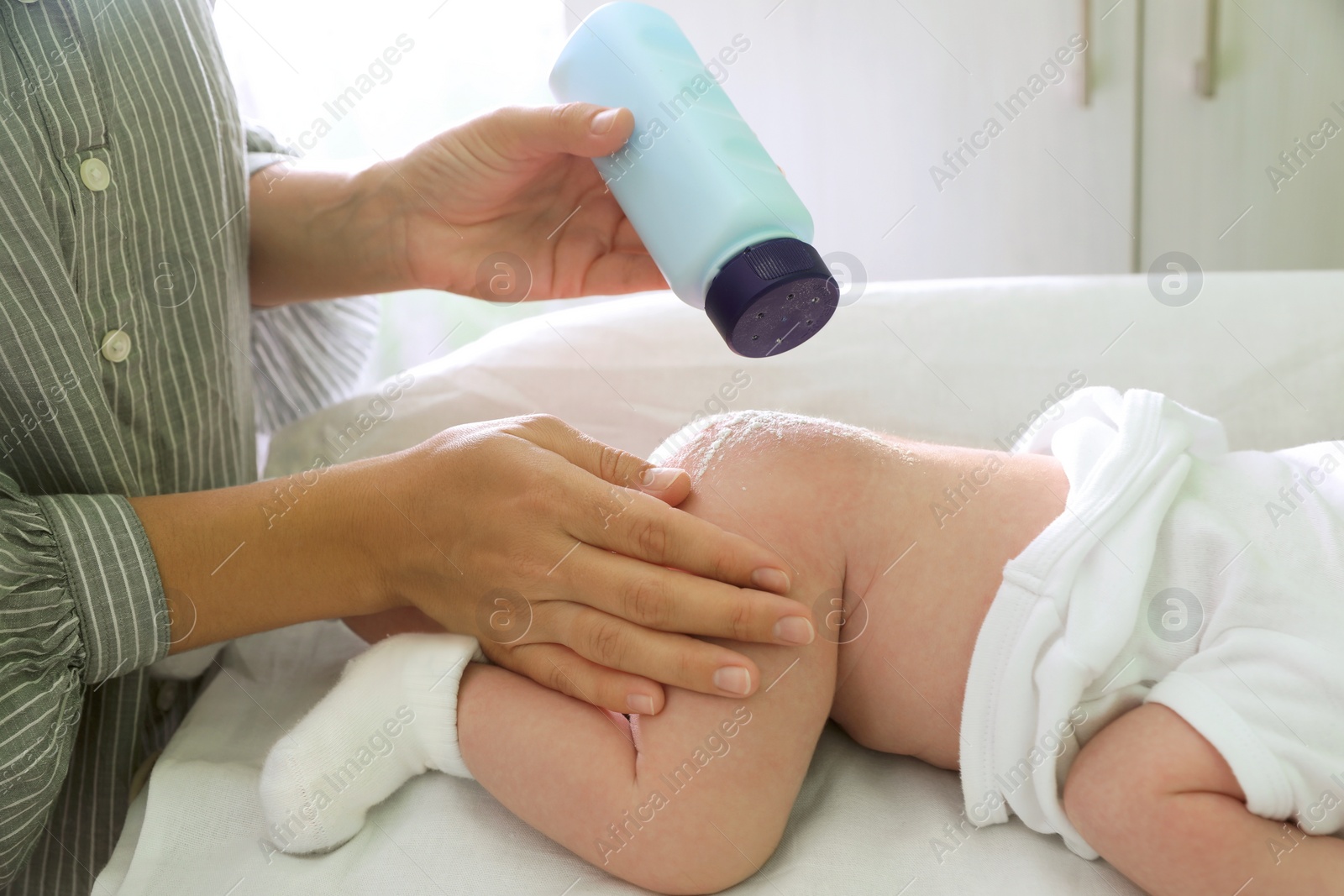 Photo of Mother applying dusting powder at baby's buttocks on changing table indoors, closeup