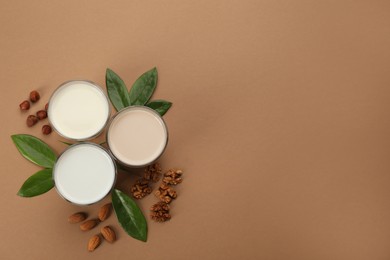 Different vegan milks and nuts on brown background, flat lay. Space for text