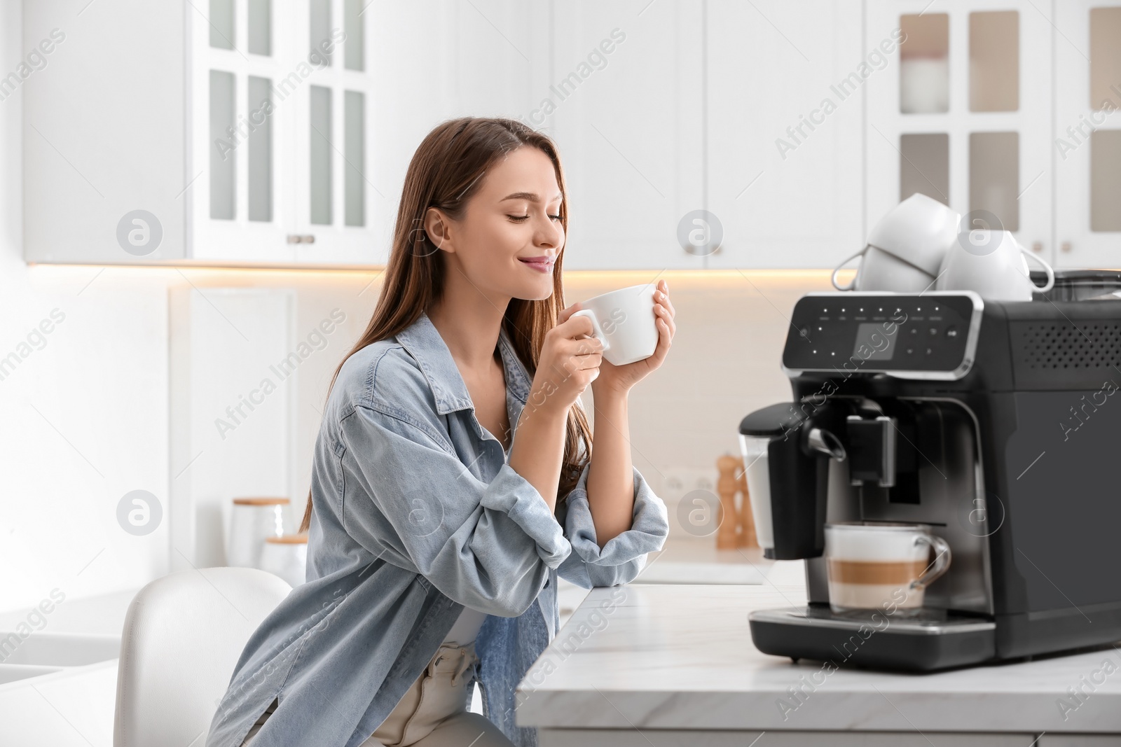 Photo of Young woman enjoying fresh aromatic coffee near modern machine in kitchen