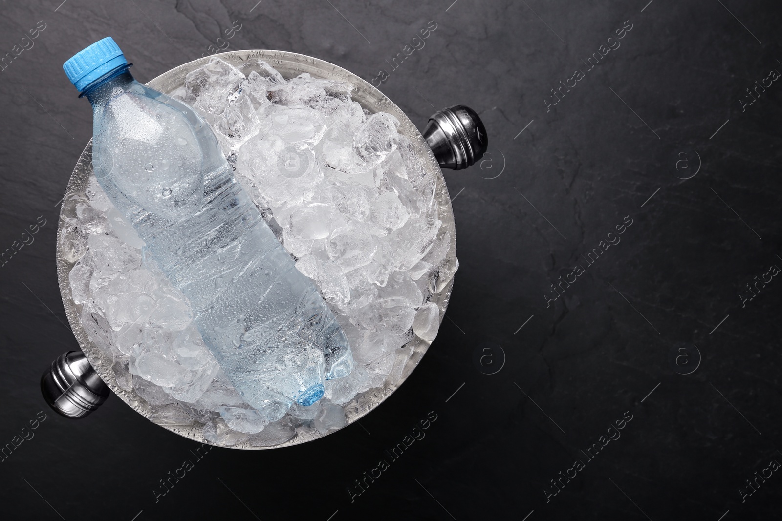 Photo of Mineral water in metal bucket with ice on black table, top view. Space for text