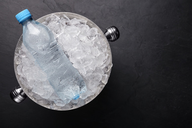 Photo of Mineral water in metal bucket with ice on black table, top view. Space for text