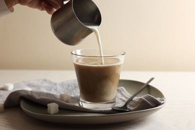 Photo of Pouring milk into cup with coffee on white wooden table, closeup