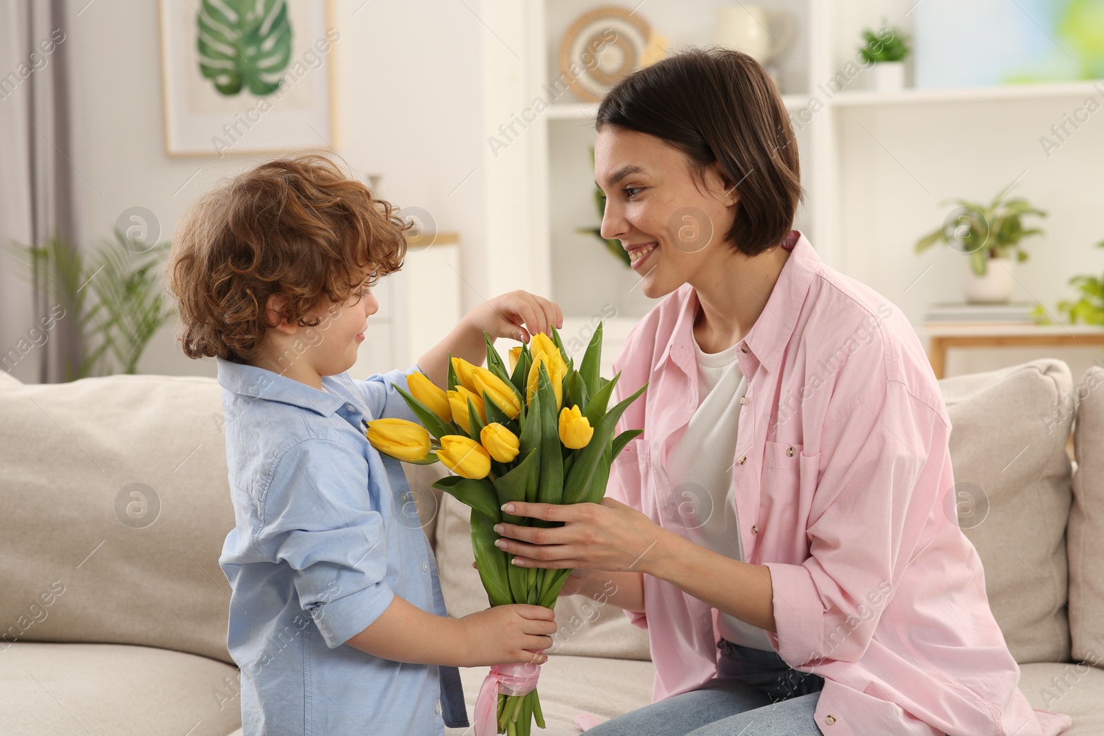 Photo of Happy woman with her cute son and bouquet of beautiful flowers at home. Mother's day celebration