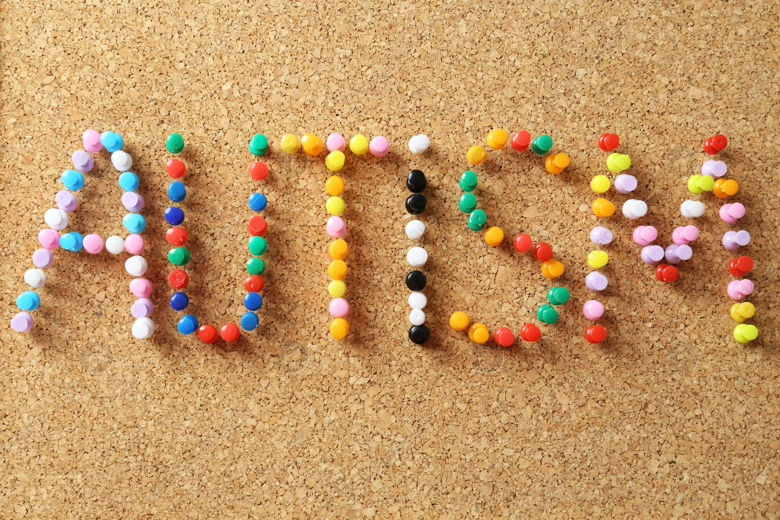 Photo of Word Autism made of colorful pins on cork board, closeup