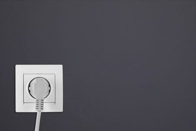 Image of Dark grey wall with power socket and inserted plug, space for text. Electrical supply