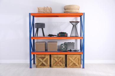 Photo of Metal shelving unit with wooden crates and different household stuff near light wall indoors