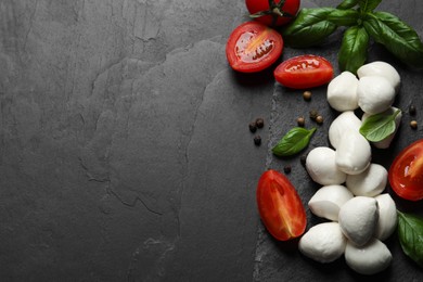 Delicious mozzarella balls, tomatoes and basil leaves on black table, flat lay. Space for text