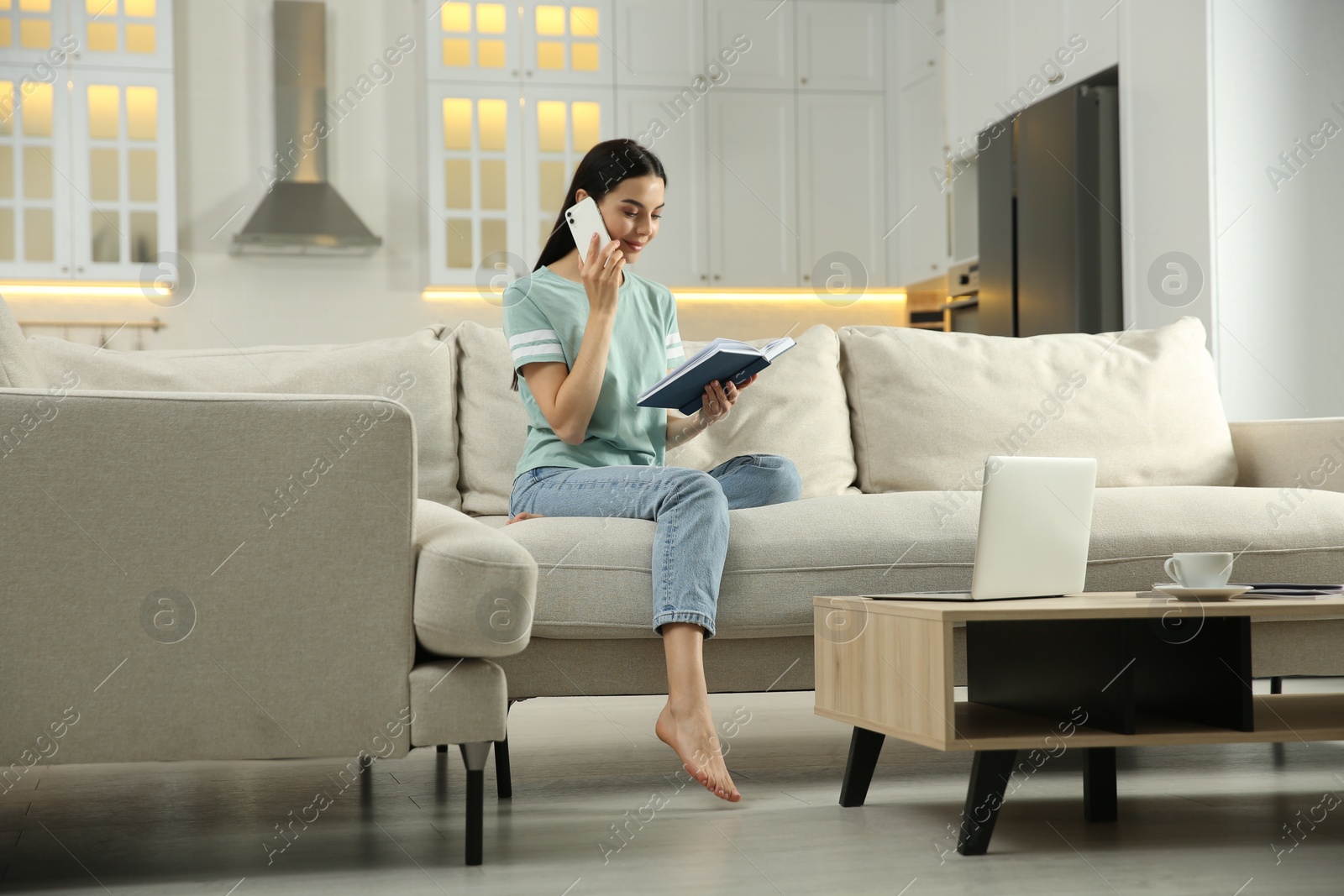 Photo of Young woman with notebook talking on phone at home