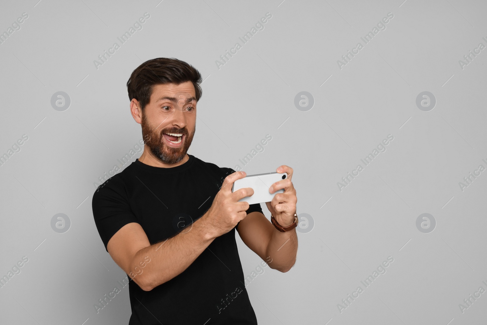 Photo of Emotional man playing game on smartphone against light background. Space for text