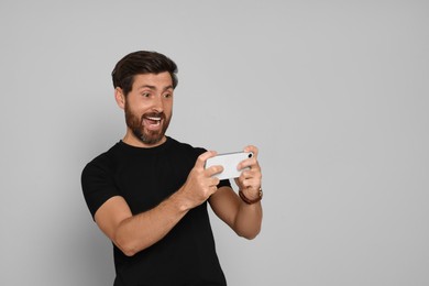 Emotional man playing game on smartphone against light background. Space for text