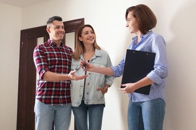 Photo of Real estate agent giving apartment keys to young couple indoors