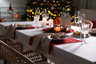 Christmas table setting with burning candles and dishware indoors