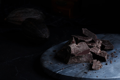 Photo of Pieces of tasty dark chocolate on grey marble board, closeup