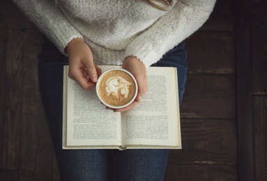 Photo of Woman with cup of coffee reading book at home, top view