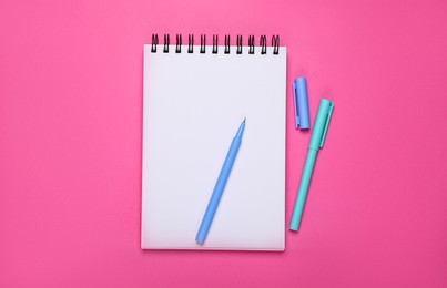 Photo of Blank notebook and pens on pink background, flat lay