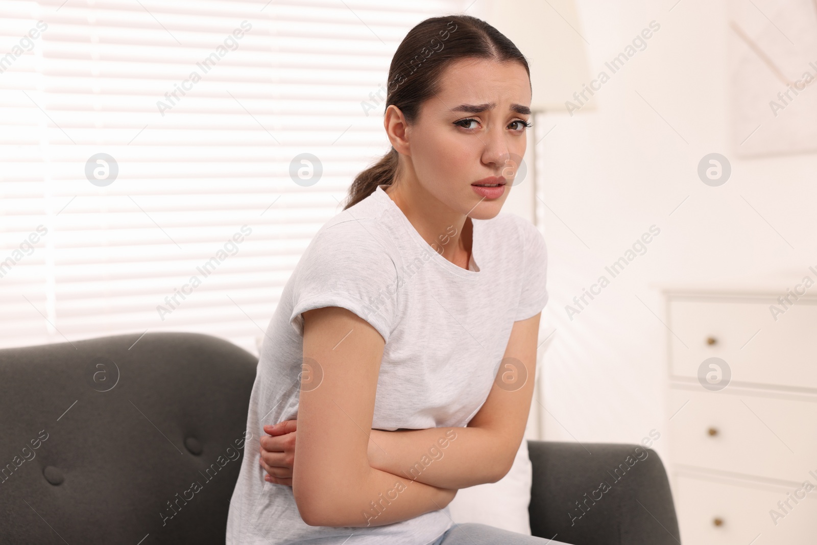 Photo of Woman suffering from abdominal pain on sofa at home. Unhealthy stomach