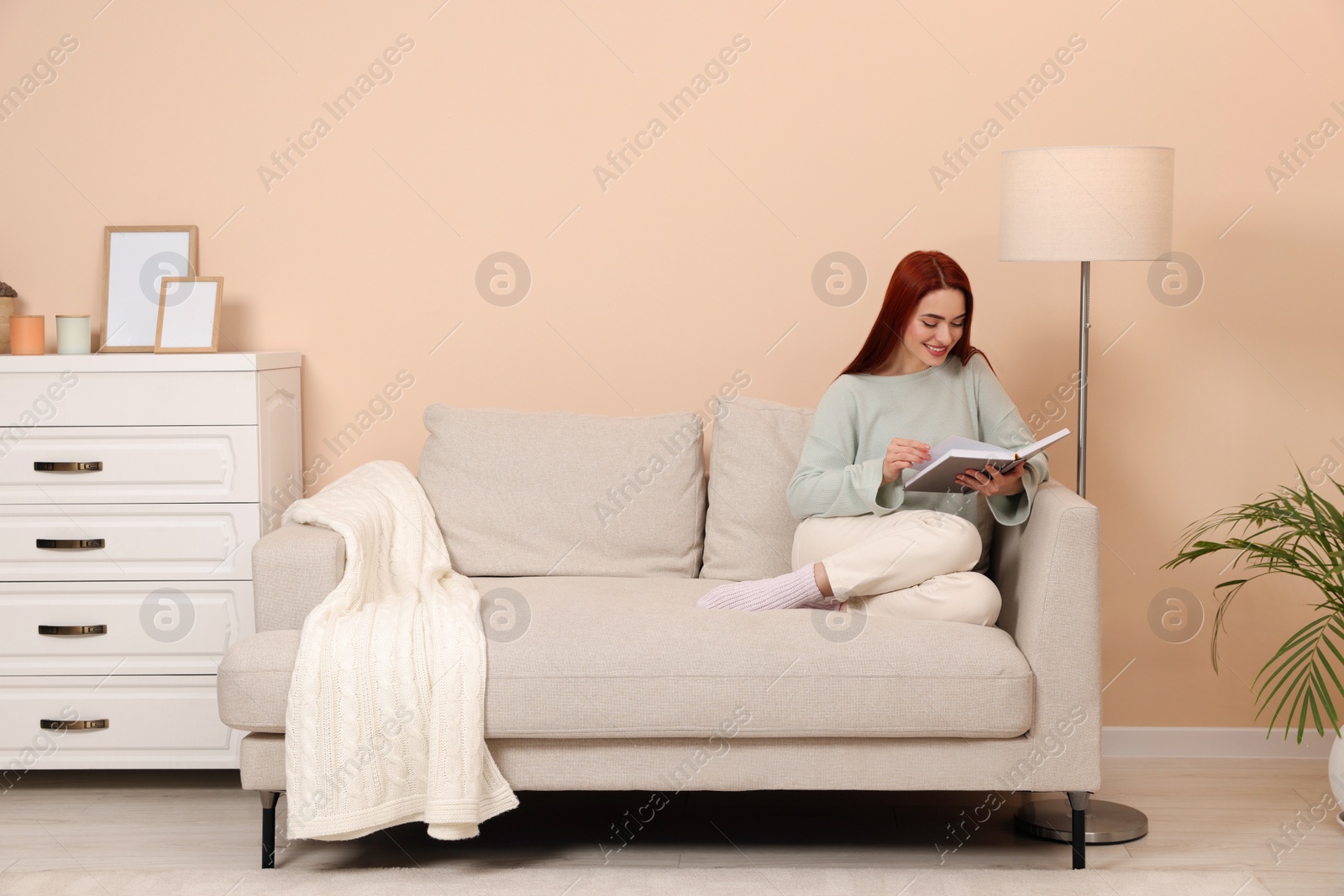 Photo of Happy woman with red dyed hair reading book at home