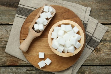 Photo of White sugar cubes in bowl and scoop on wooden table, top view