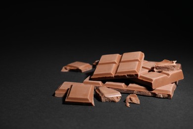 Photo of Pieces of delicious milk chocolate bars on black background