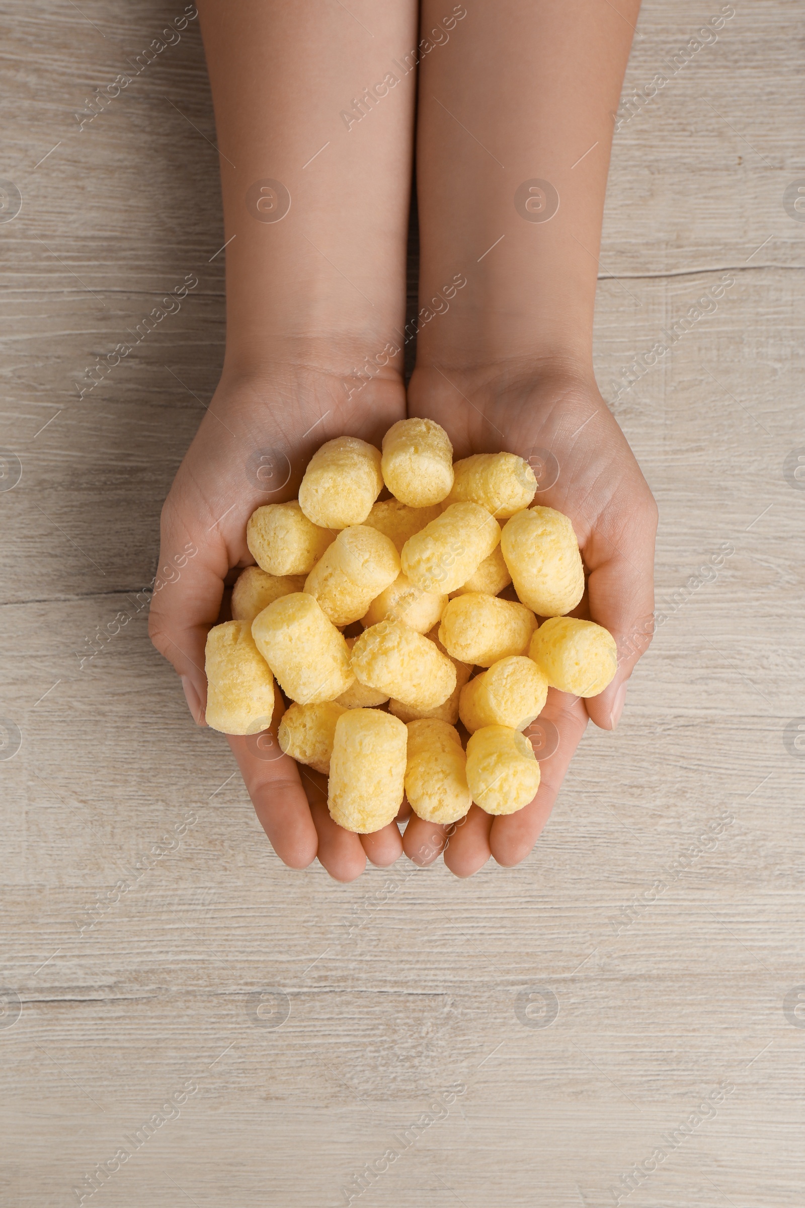 Photo of Woman holding corn sticks at wooden table, top view