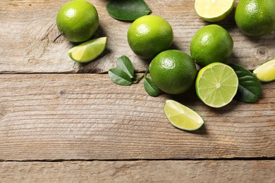 Photo of Fresh limes and green leaves on wooden table, flat lay. Space for text