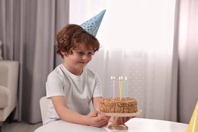 Cute boy with birthday cake at table indoors