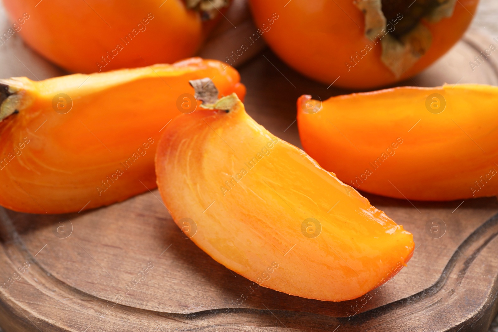 Photo of Whole and cut delicious ripe persimmons on wooden table, closeup