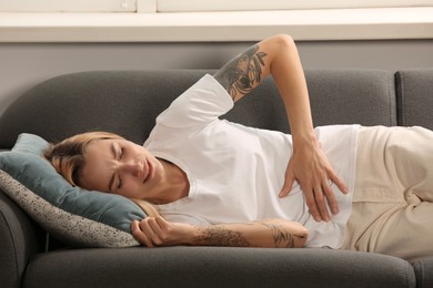 Photo of Young woman suffering from menstrual pain on sofa indoors