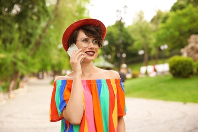 Photo of Young woman in stylish outfit talking on phone outdoors
