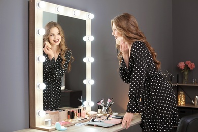 Young woman applying makeup near mirror in dressing room