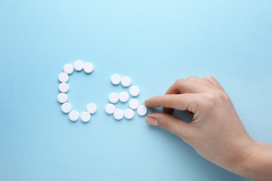 Woman making calcium symbol with white pills on light blue background, top view