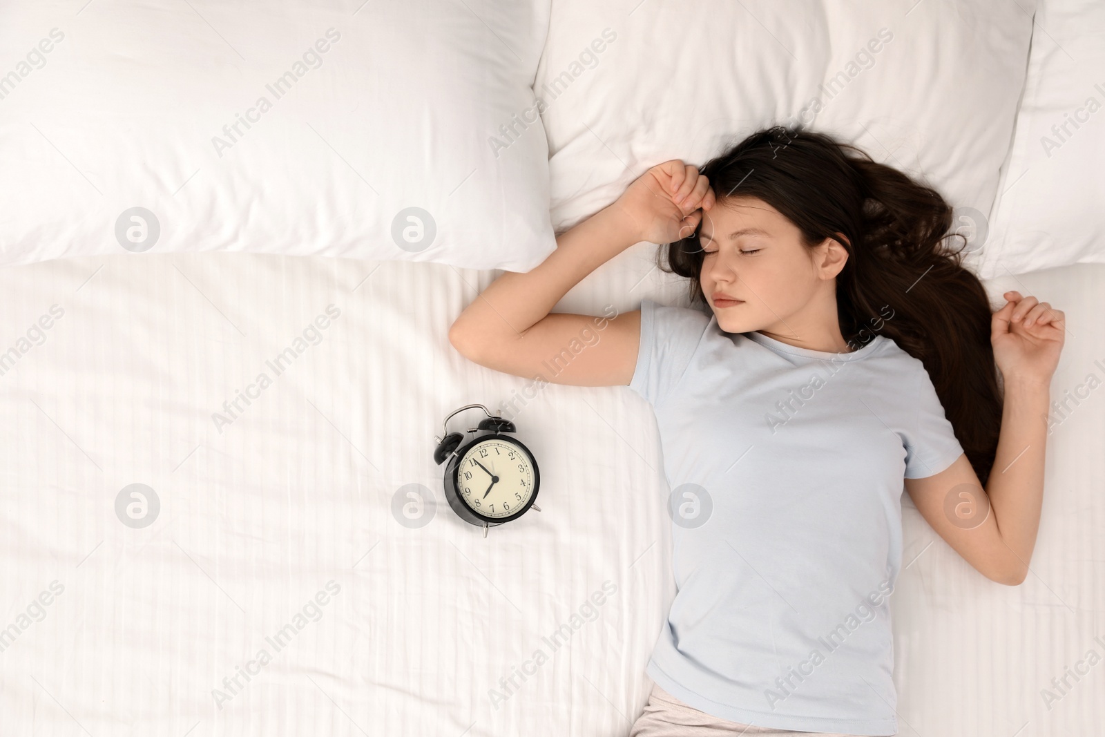 Photo of Beautiful little girl with alarm clock sleeping in bed, top view. Space for text