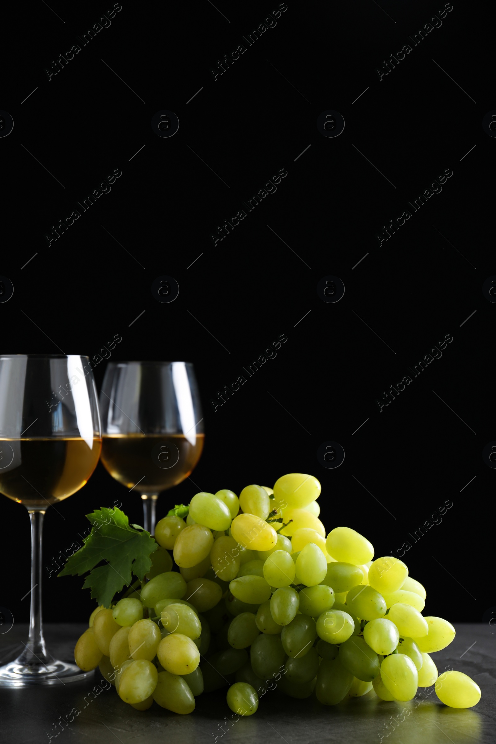 Photo of Fresh ripe juicy grapes with wineglasses on grey table against black background, space for text