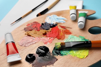 Photo of Palette, tubes of oil paints, brushes and canvas on light blue background, closeup