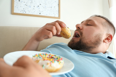 Photo of Lazy overweight man eating donuts at home, closeup