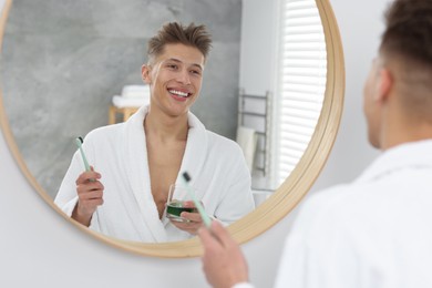 Photo of Young man using mouthwash near mirror in bathroom