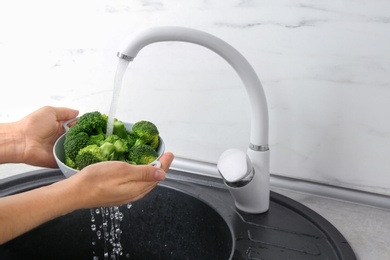Photo of Woman washing bowl of fresh green broccoli in kitchen sink, closeup view