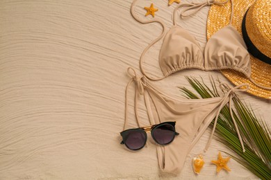 Stylish bikini and beach accessories on sand, flat lay. Space for text