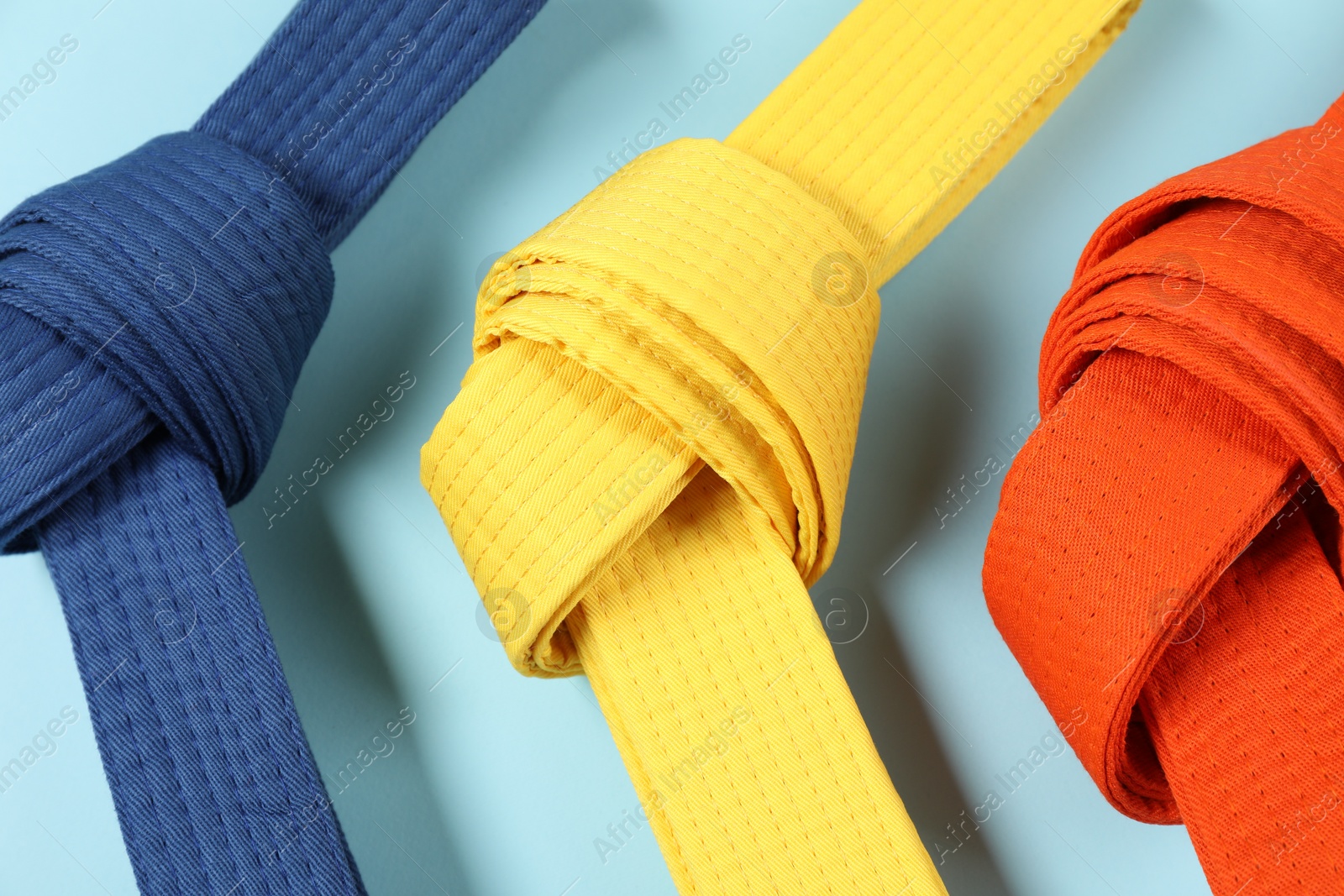 Photo of Colorful karate belts on light blue background, flat lay