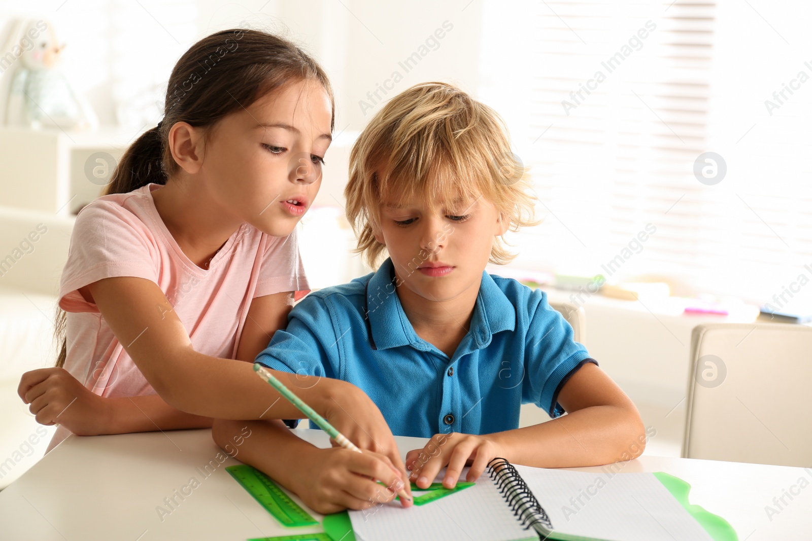 Photo of Little boy and girl doing homework at table indoors