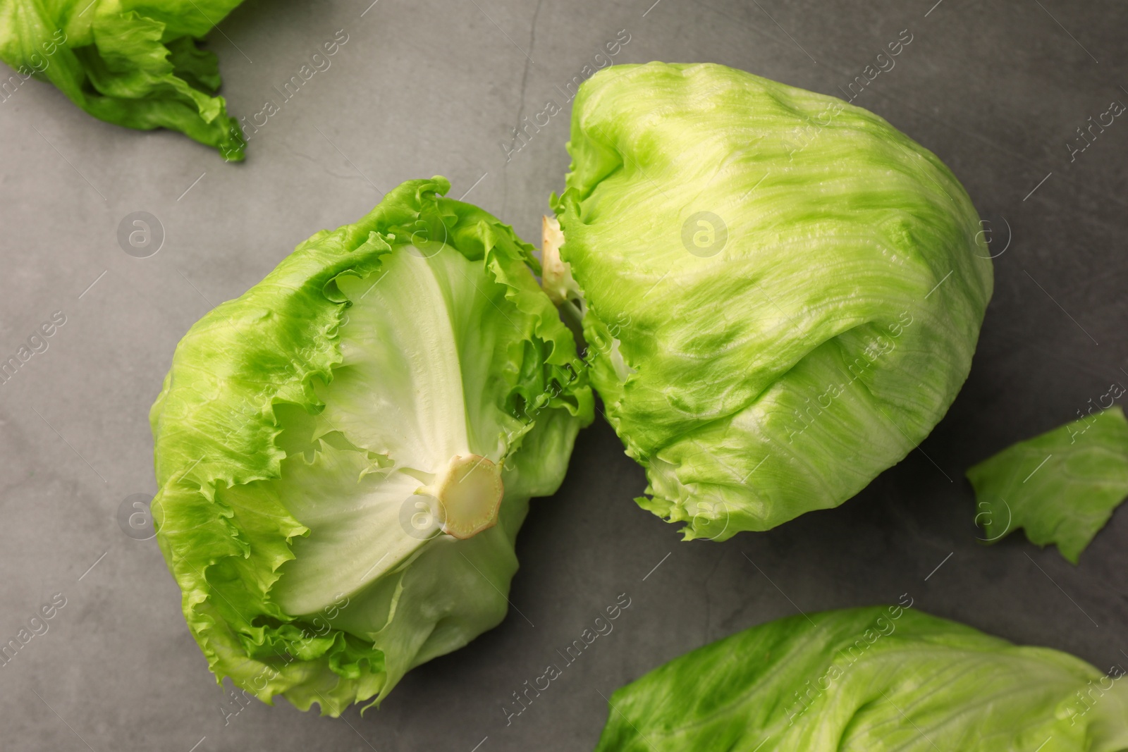 Photo of Fresh green iceberg lettuce heads and leaves on grey table, flat lay